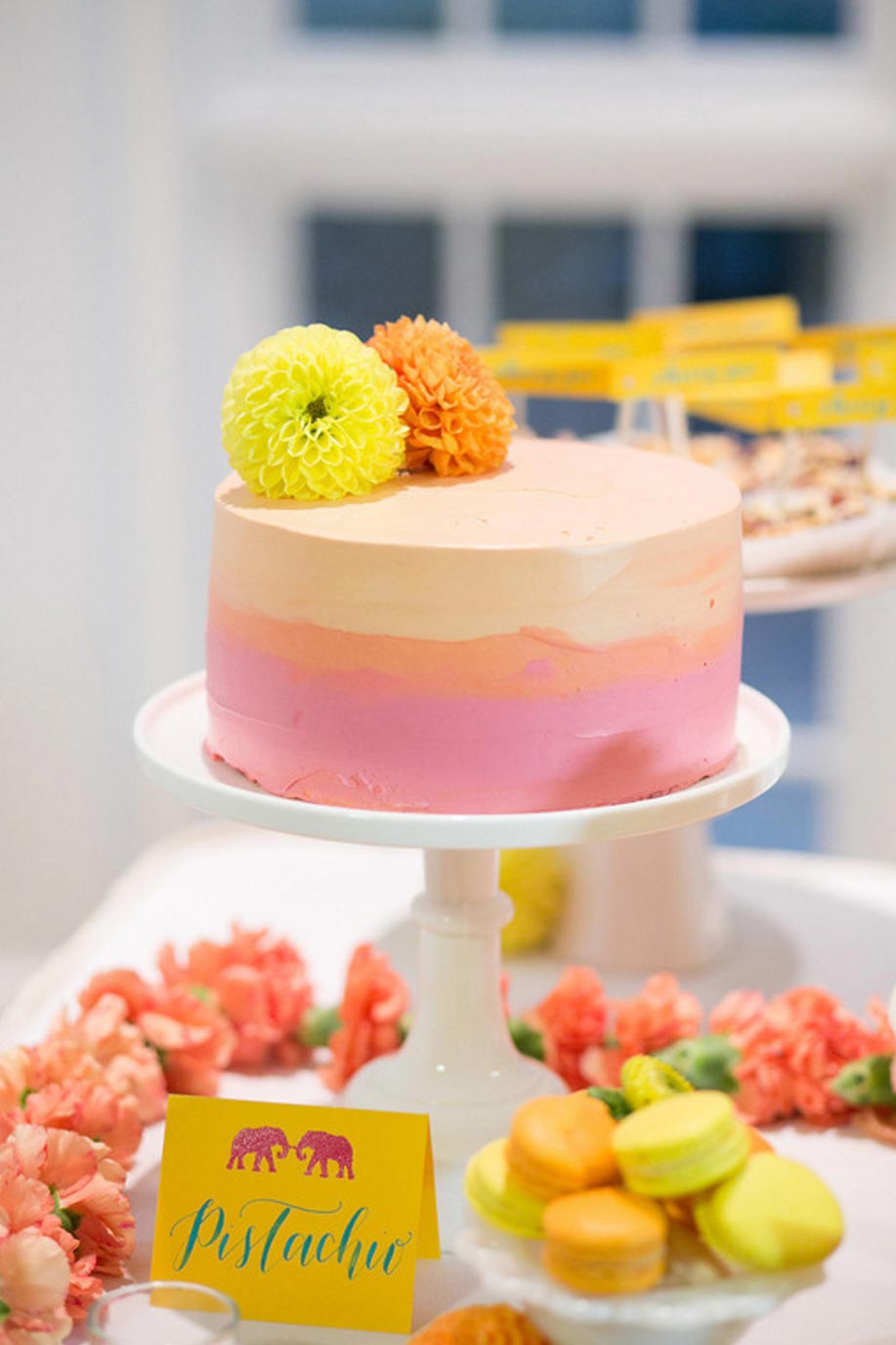 Buttercream wedding cake and colorful macarons and yellow calligraphy place card with elephants