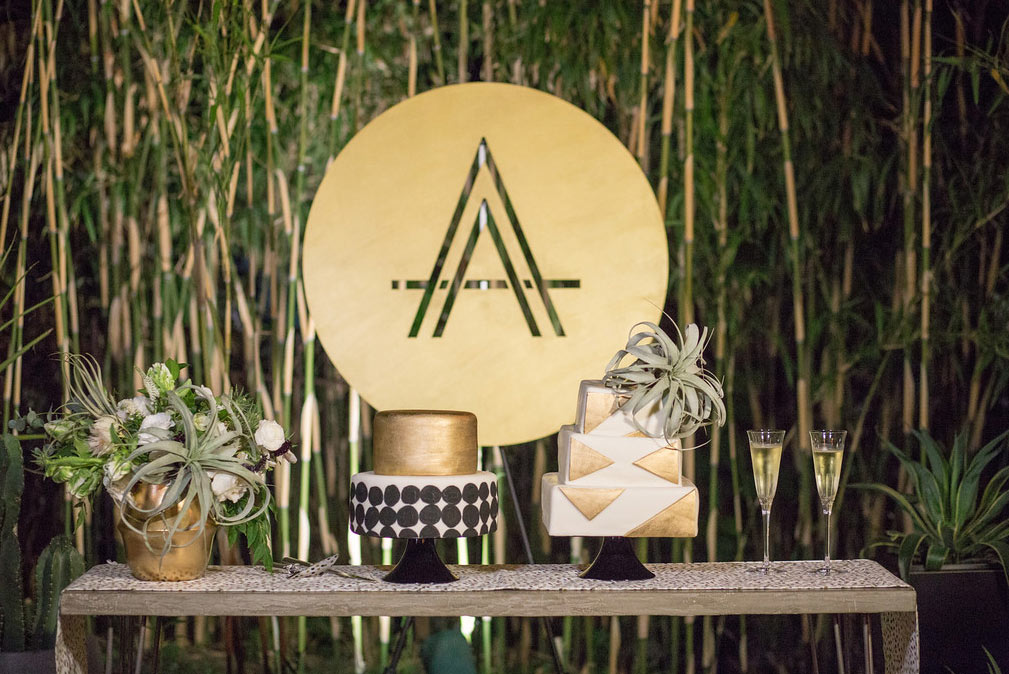 Black, white, and gold dot and triangle shape wedding cakes with custom laser cut wood circle monogram sign at The Hotel Belmont