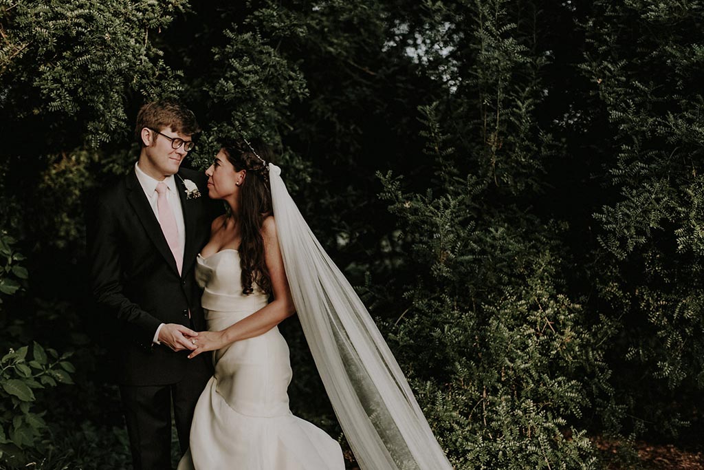 Bride and groom take an elegant wedding day portrait in front of greenery at Texas Discovery Gardens in Dallas