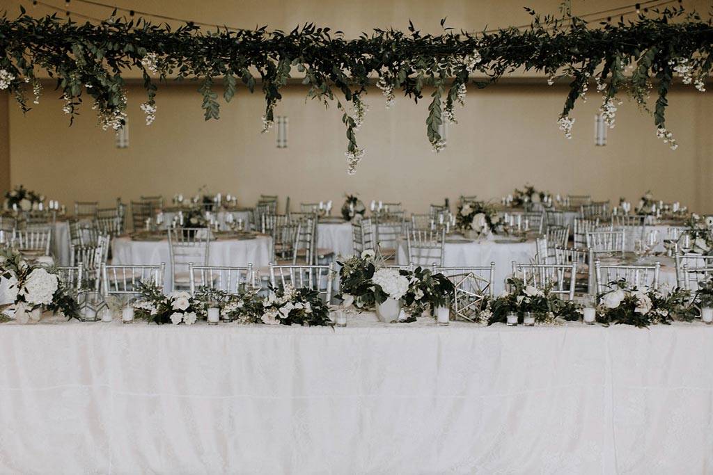 Long wedding head table with hanging organic greenery installation at Texas Discovery Gardens in Dallas